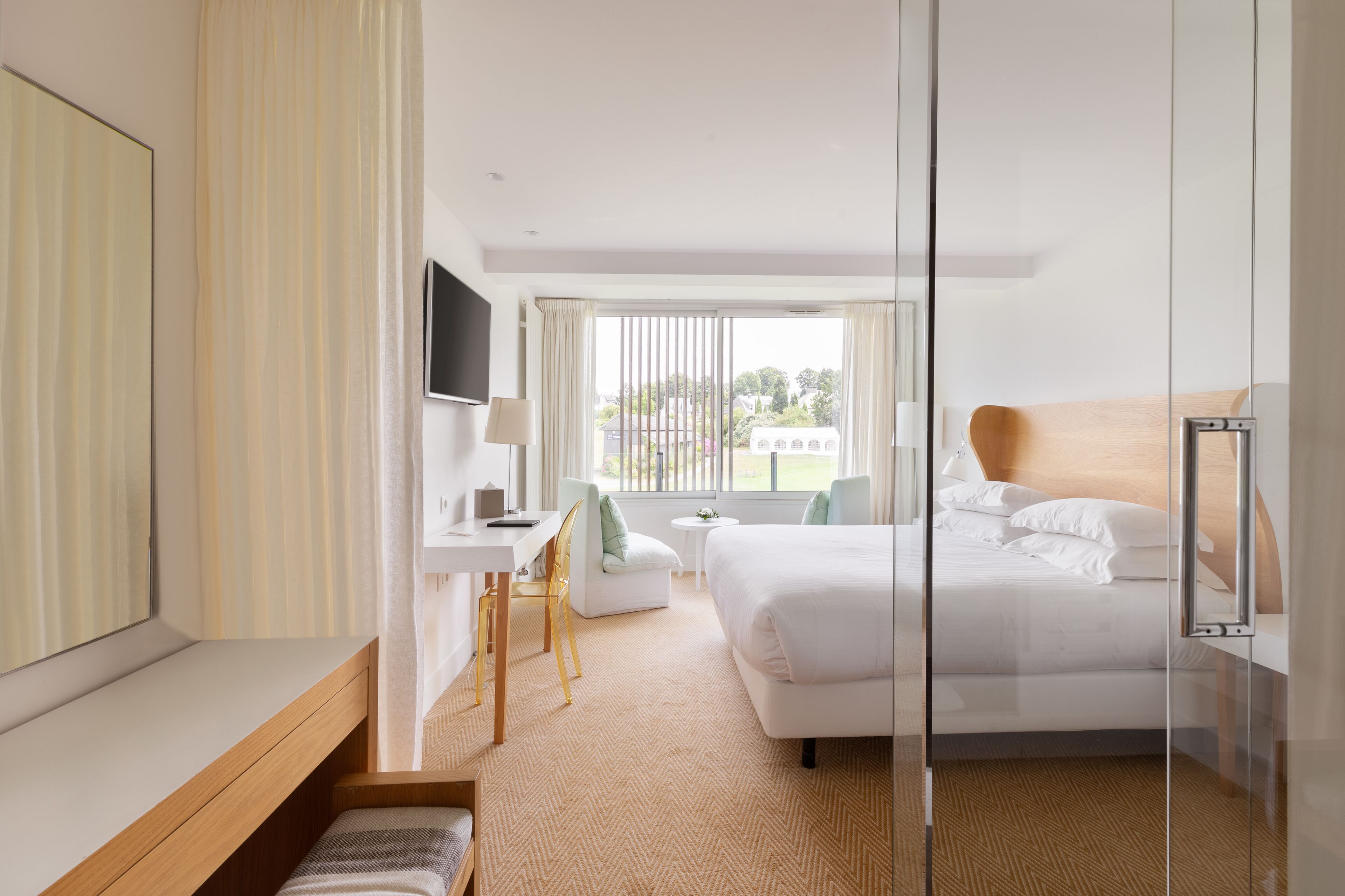 Une chambre d’hôtel équipée d’un lit, d’un bureau, d’une chaise, d’une télévision et d’une fenêtre donnant sur l’extérieur.