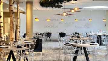 A restaurant with clear glass tables and chairs, a stone floor, and a wall with the name 'GUESTHOUSE' and 'ESCALABUR' visible.