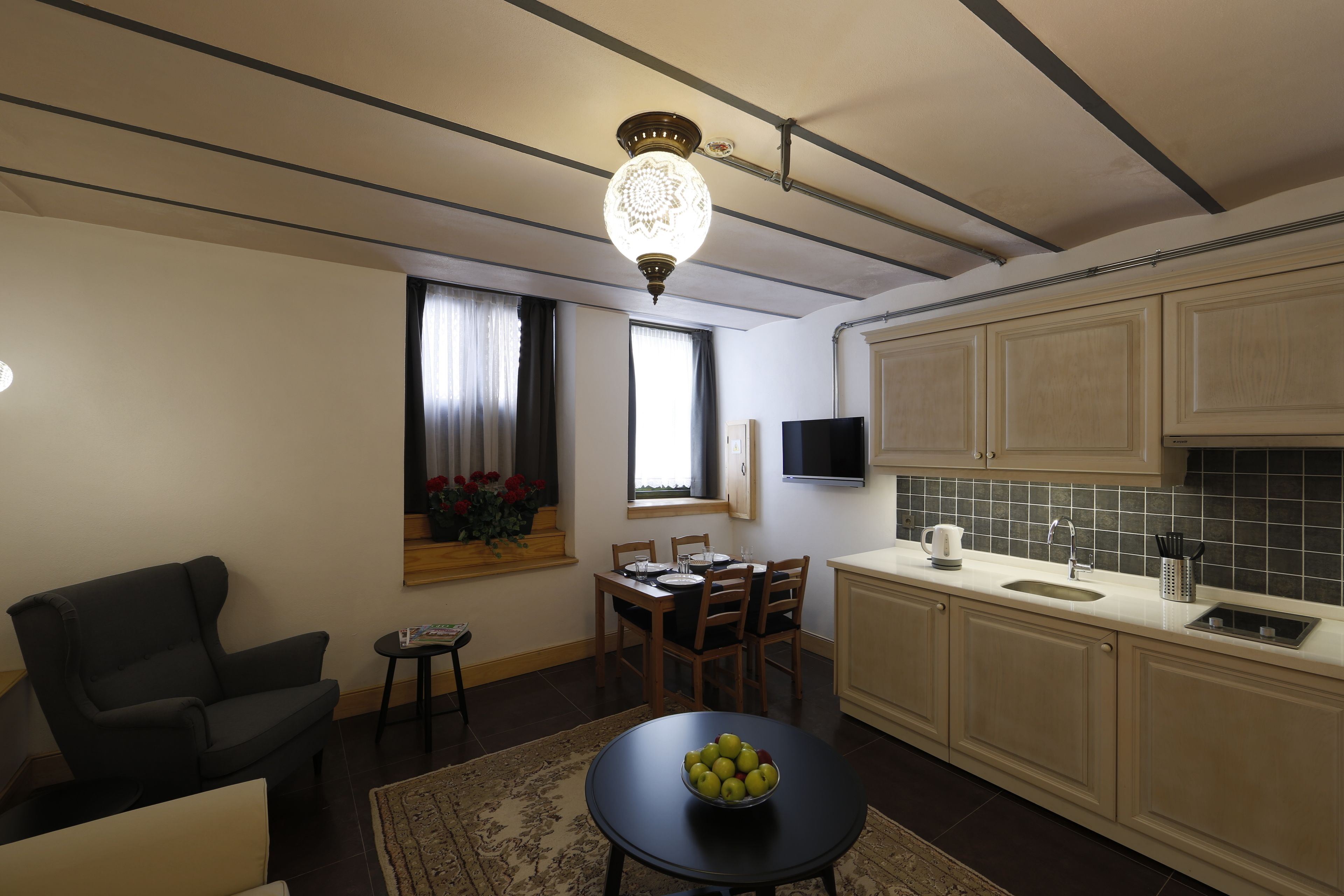 A compact living space with a dining area, a kitchen with a sink and stove, and a ceiling with exposed beams.