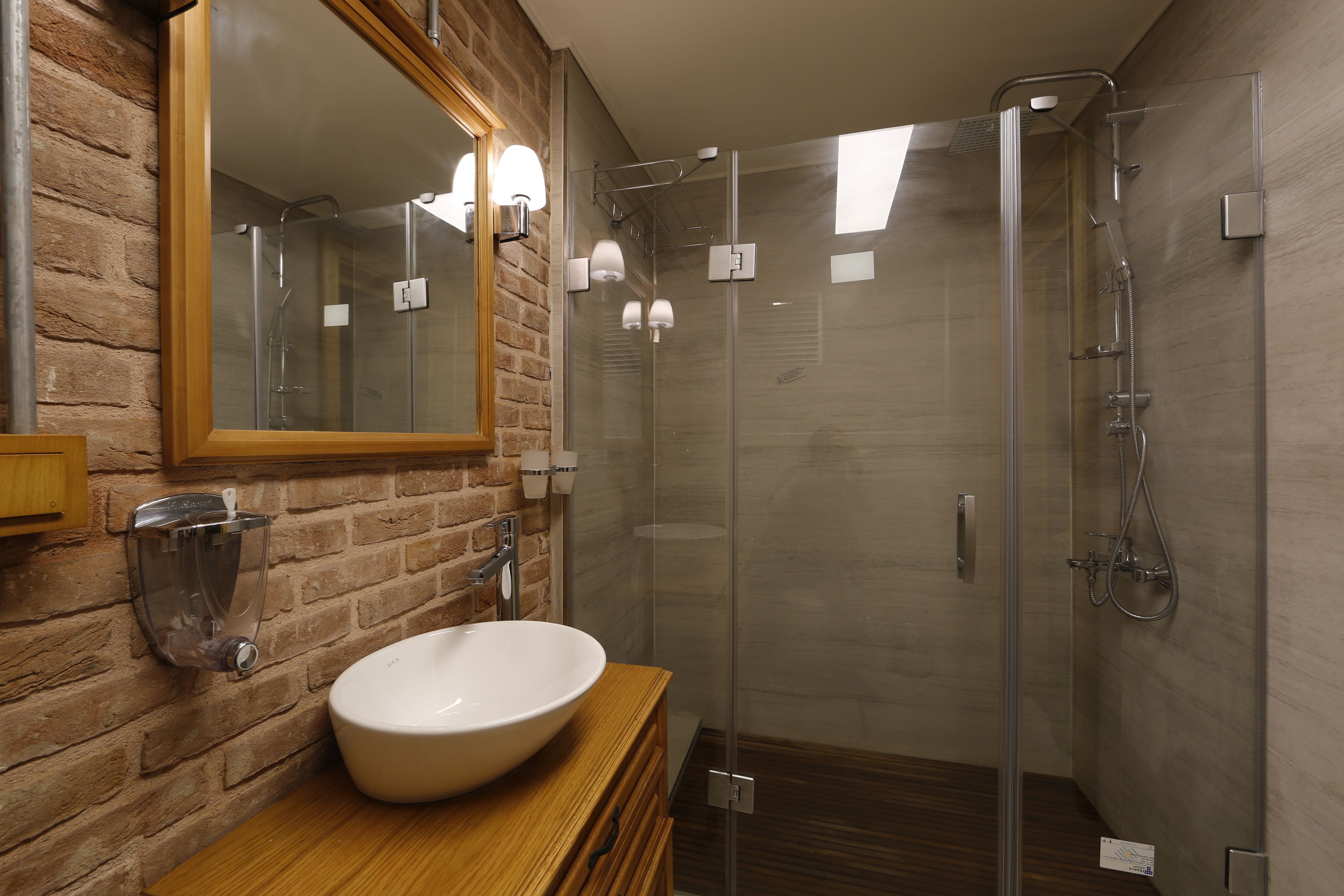 A modern bathroom with a large mirror, a wooden vanity, a white sink, and a glass-enclosed shower area.