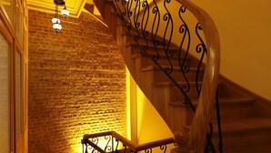 Un escalier en colimaçon, doté de rampes en métal ouvragé et de marches en bois, menant à un palier où est fixée une applique murale.