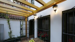 Une table en bois avec un saladier de pommes et une chaise, une pergola en bois et une fenêtre ornée de fleurs rouges.