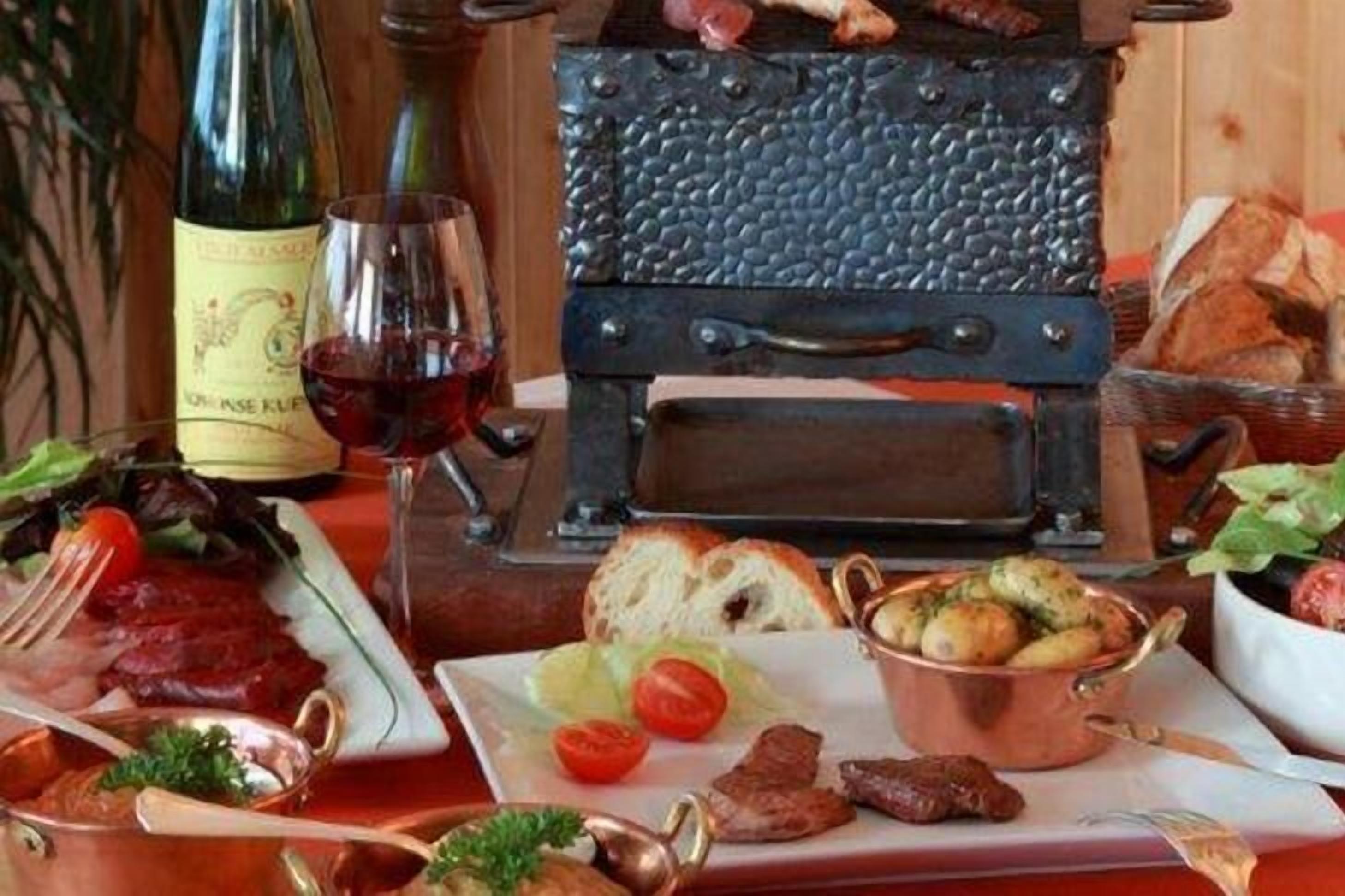 Una mesa de comedor con una botella de vino, una copa y diversos platos, incluyendo carne, pan y verduras.