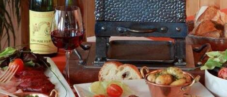 Una mesa de comedor con una botella de vino, una copa y diversos platos, incluyendo carne, pan y verduras.