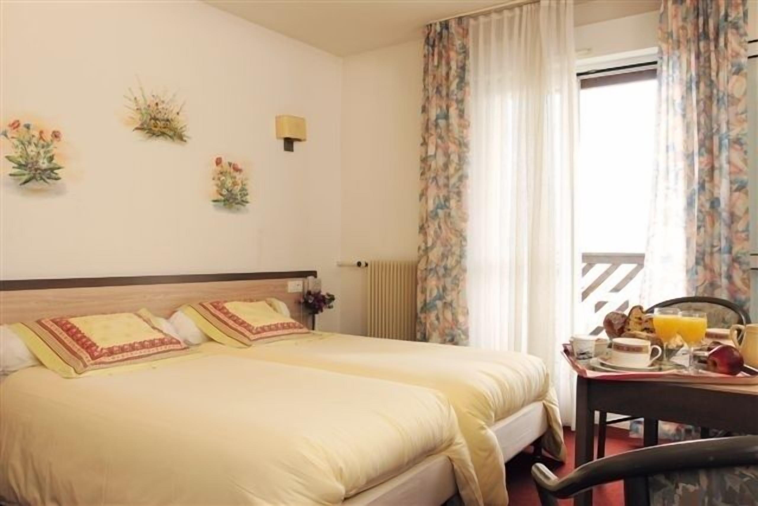 A hotel room with a double bed, a small table with breakfast items, and a window with curtains.