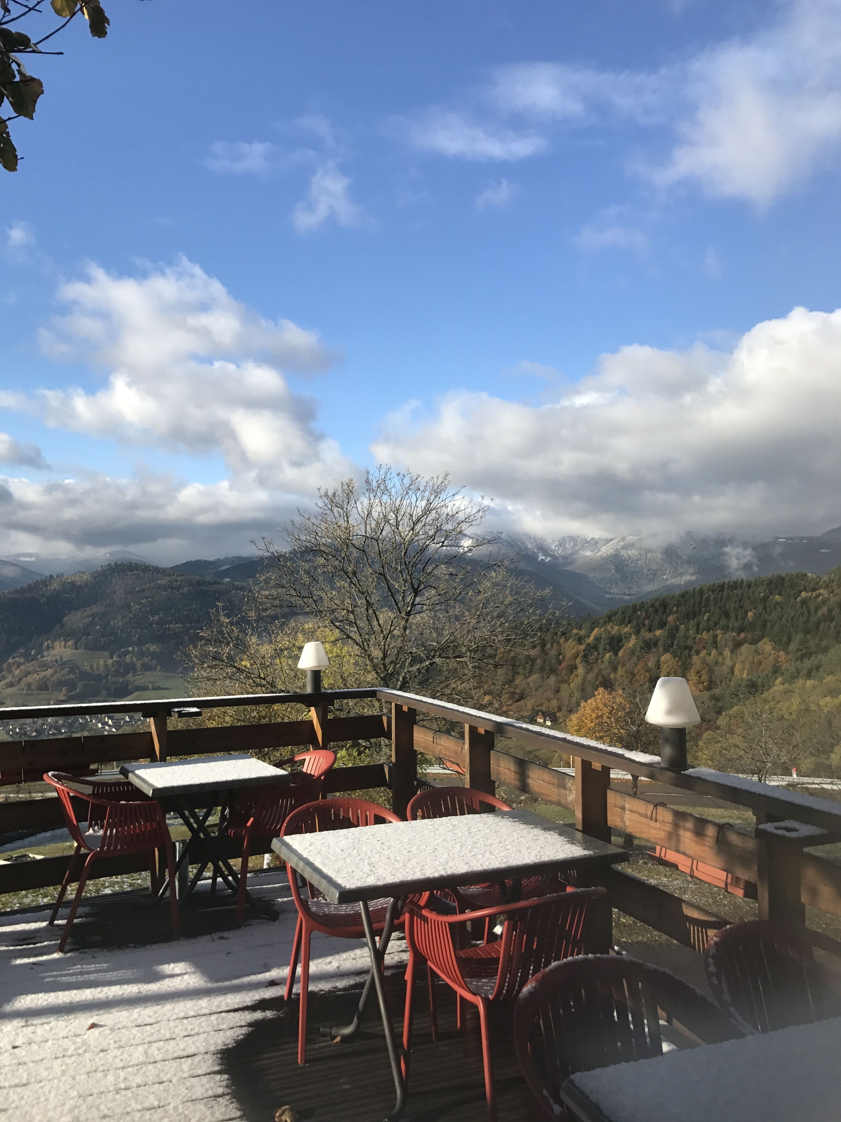 Une terrasse en bois, agrémentée de tables et de chaises, qui offre une vue imprenable sur un paysage montagneux, avec des sommets enneigés et un ciel dégagé.