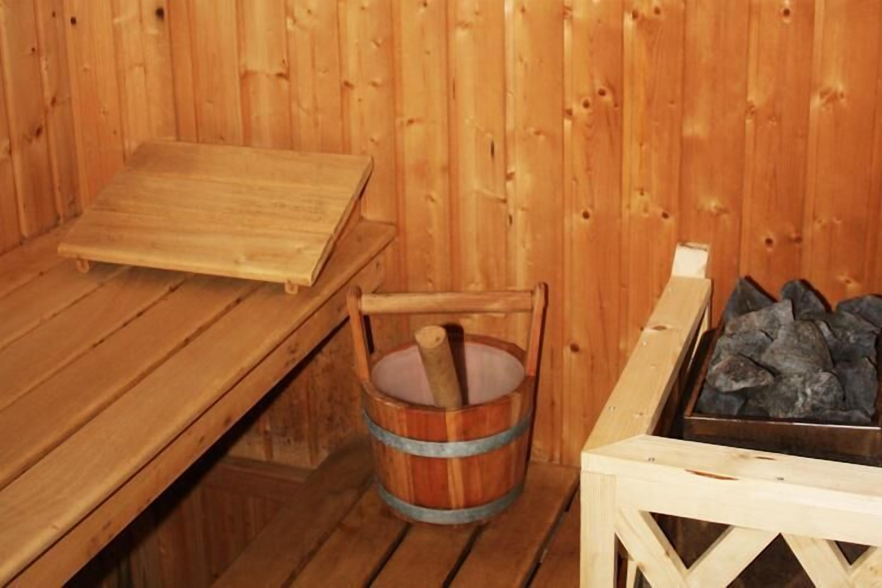 Sauna de fusta amb una panxa, un cubet de fusta i un recipient metàl·lic amb pedres.