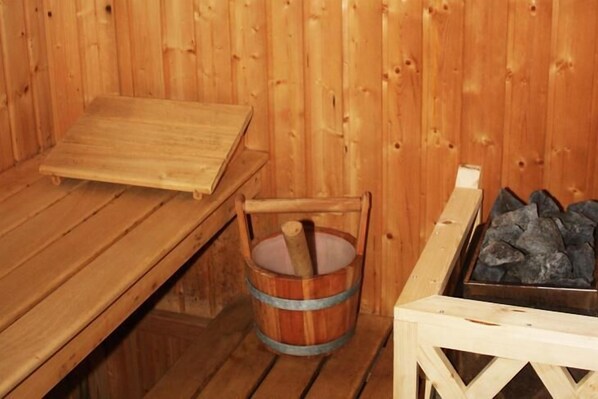 A wooden sauna with a bench, a wooden bucket, and a metal container with stones. - Hôtel - Restaurant Panorama (Hohrod)