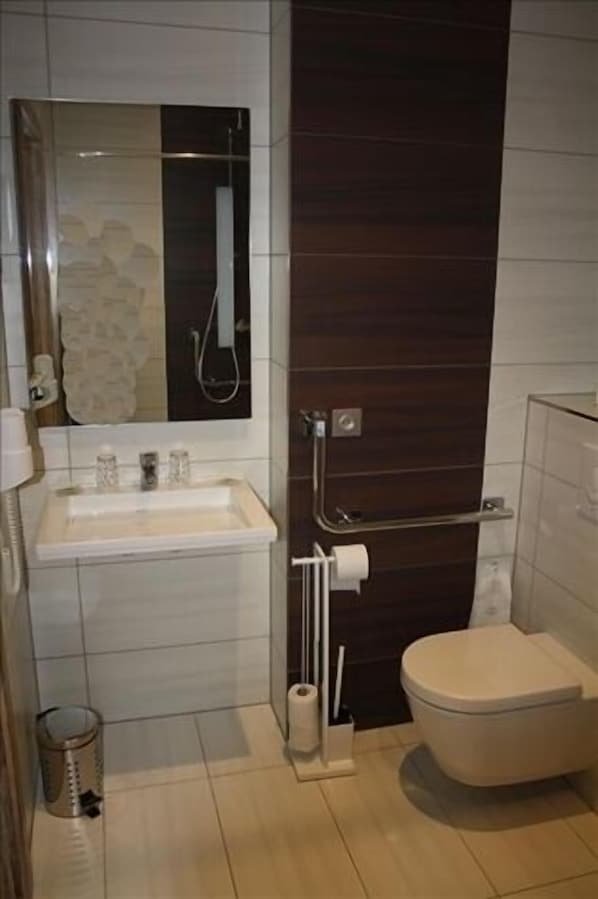 A small bathroom with a sink, mirror, toilet, and shower. - Hôtel - Restaurant Panorama (Hohrod)