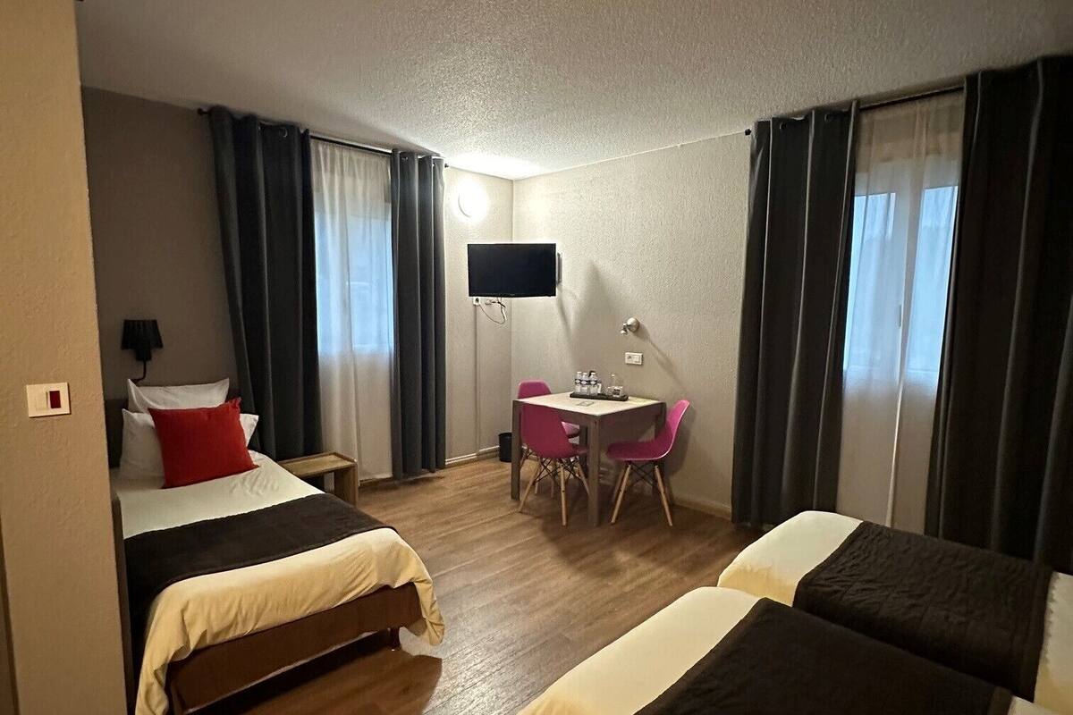Hotellihuone, jossa on kaksi sänkyä, työpöytä, tuoli, televisio ja ikkuna, jossa on verhot.