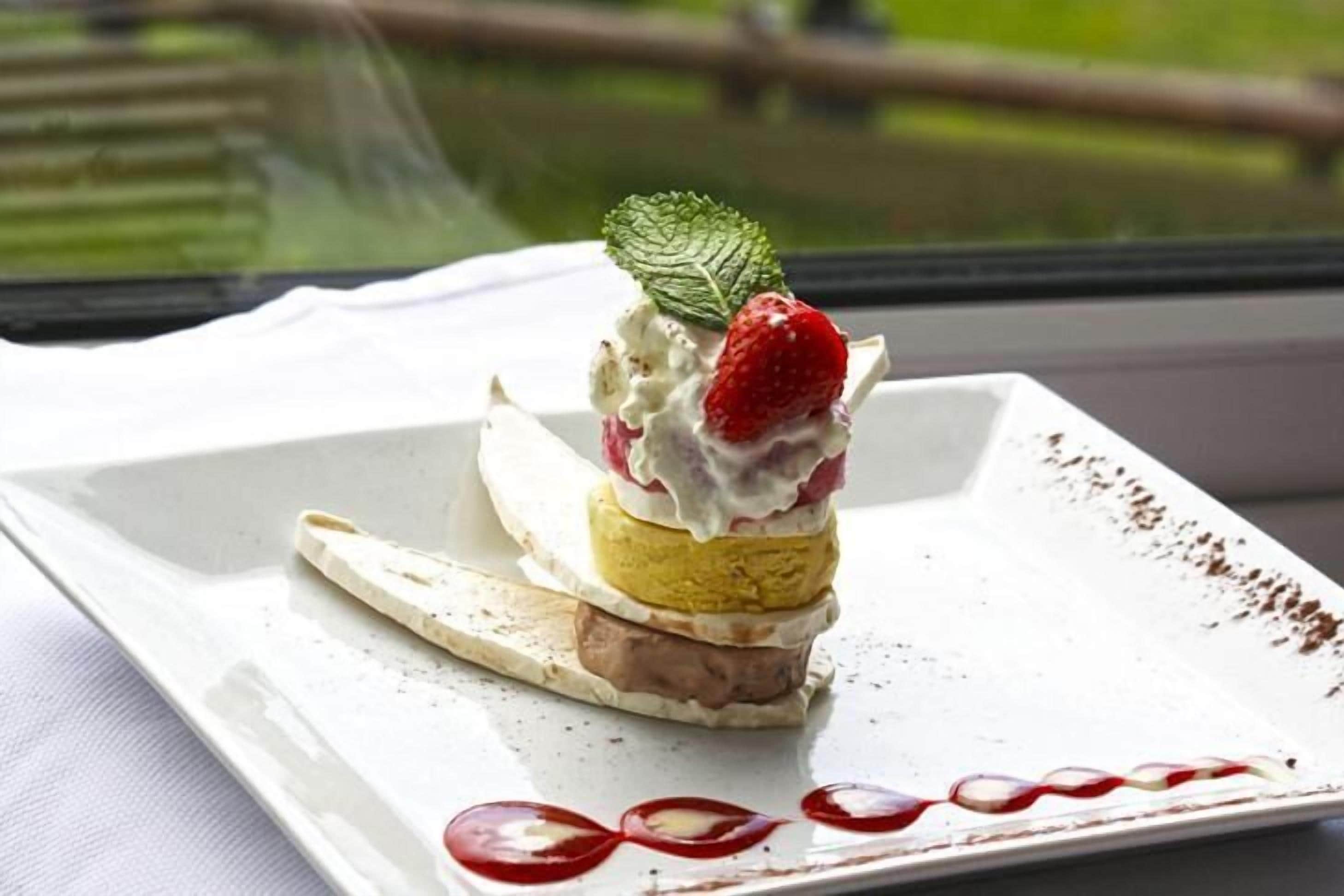 Un dessert servi dans une assiette blanche, avec une vue sur une fenêtre en arrière-plan.