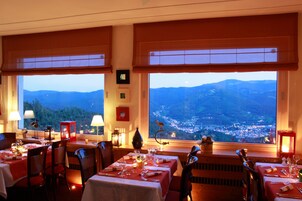 A restaurant with tables set for dining, large windows offering a view of a mountainous landscape, and warm lighting.