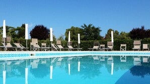 A clear blue pool with lounge chairs and umbrellas, surrounded by greenery.
