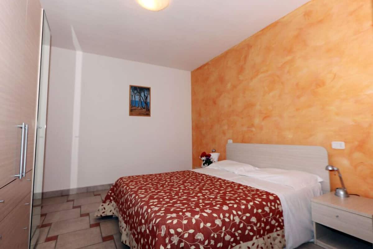 Una habitación de hotel con una cama, una mesita de noche, una lámpara, un cuadro en la pared y un armario de madera.