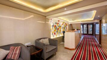 A hotel lobby with a marble floor, a red and black striped carpet, a reception desk, and a wall with a colorful geometric pattern.