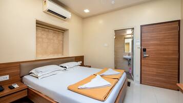 A hotel room with a bed, bedside tables, an air conditioner, a wooden door, and a bathroom visible through an open door.