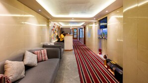 Et hotellobby med en receptionsdisk, en sofa med puder, et mønstret tæppe og et fjernsyn på væggen.