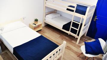 Habitación con literas, una cama individual, una silla y una pequeña mesa con una planta.