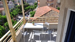 A balcony with a table and chairs, a potted plant, and a view of a cityscape with buildings and trees. - Hostal Porto Mar (Salou)