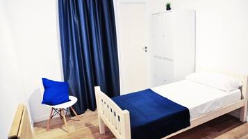 Een kleine, verzorgde slaapkamer met een enkel bed, een stoel, een garderobe en een radiator.