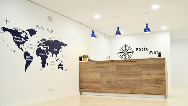 A reception desk with a wooden finish, a world map on the wall, and a compass. - Hostal Porto Mar (Salou)