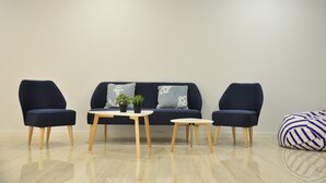 A modern living room with a dark blue sofa, two matching armchairs, a small wooden coffee table, and a round side table. - Hostal Porto Mar (Salou)