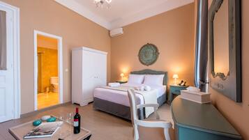 Quarto de hotel com cama, mesa de cabeceira, cadeira e uma mesa com garrafa de vinho e copos.