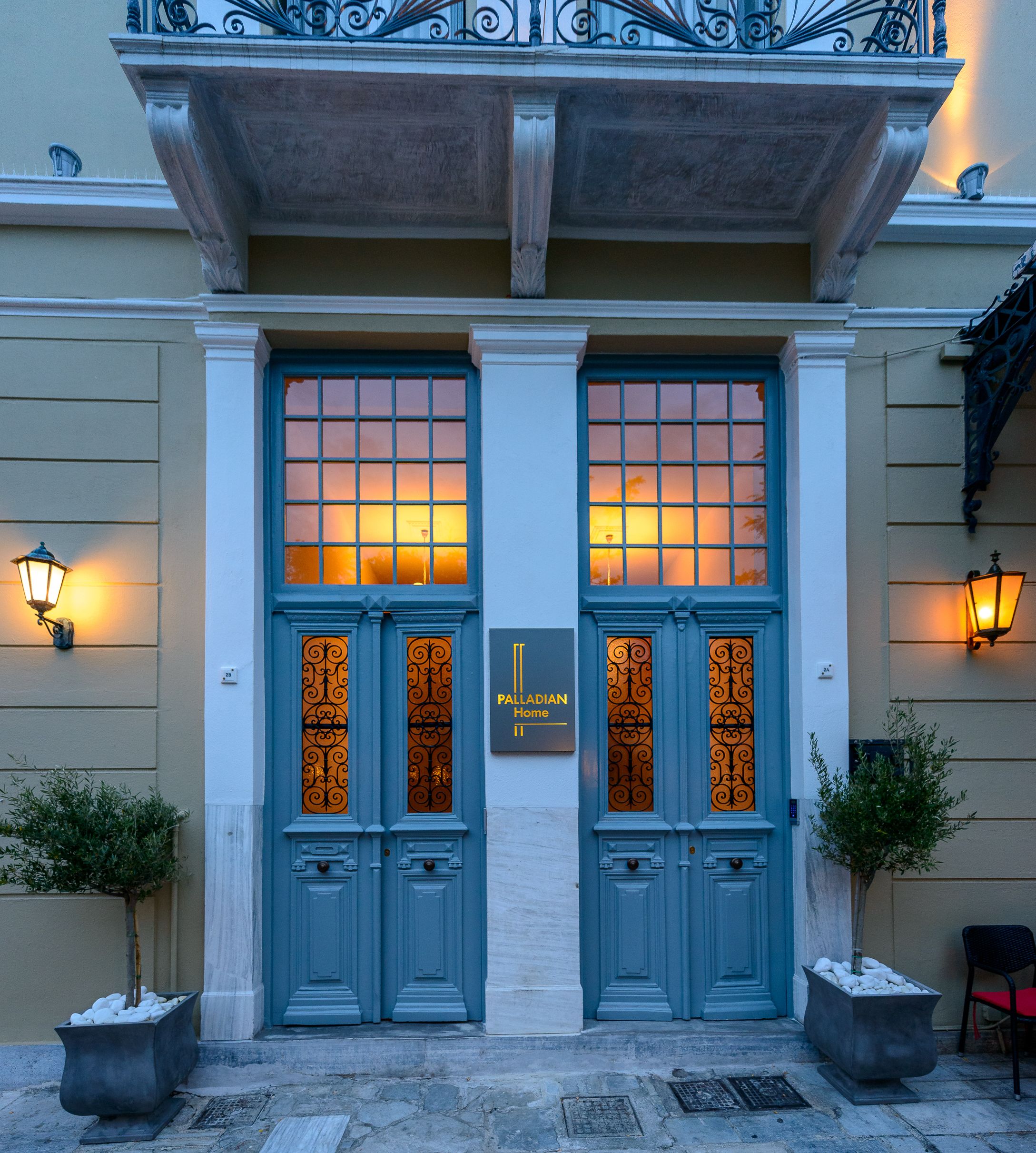 L'ingresso di un edificio con due porte blu, una targa con su scritto "Palladian Home" e due piante in vaso ai lati.