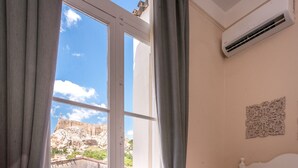 A hotel room with a large window, a bed with white linens, and a view of a rocky landscape. - Palladian Home (Athens)