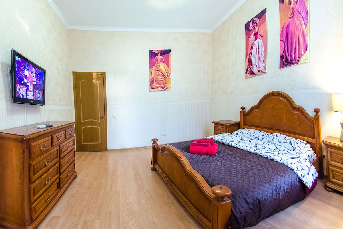 A bedroom with a wooden bed, a dresser, a television, and wall art.
