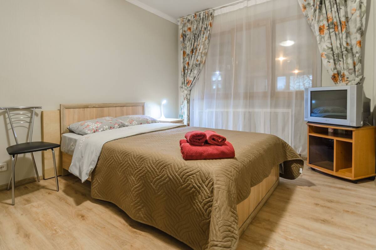 A bedroom with a bed, a chair, a TV, and curtains.