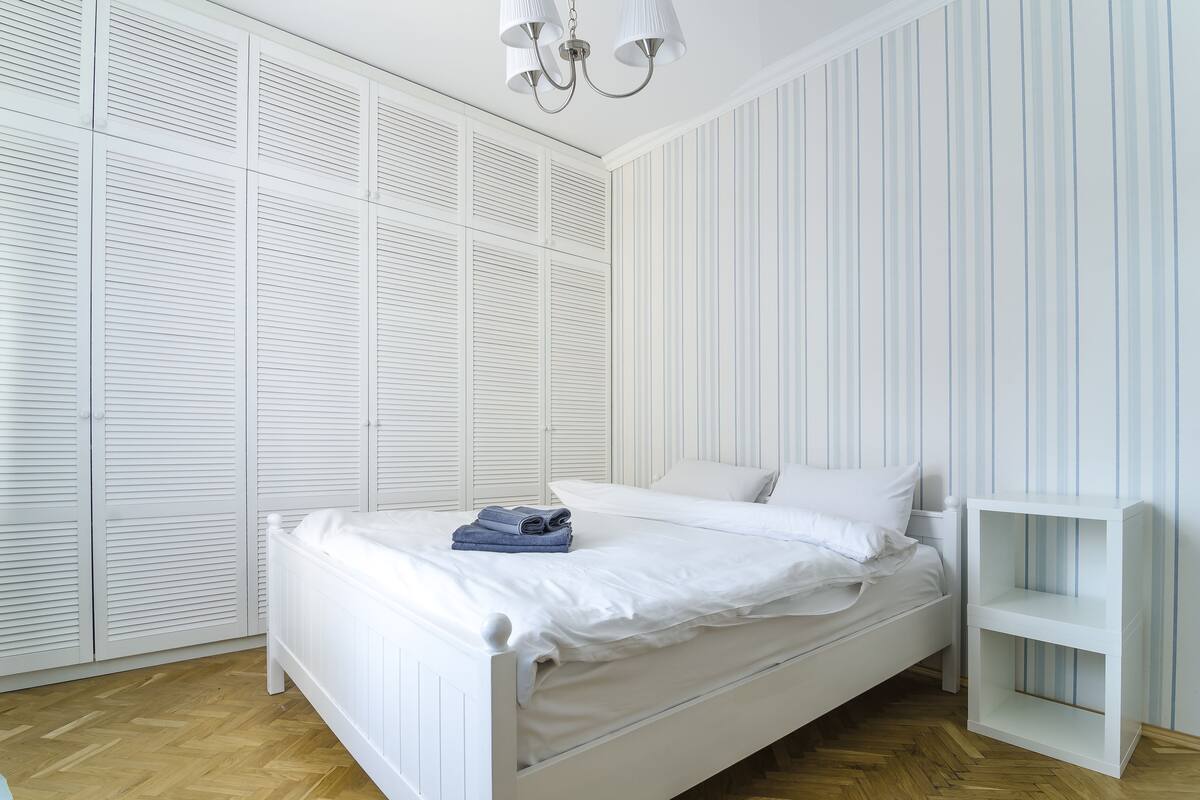 A bedroom with a white bed, a nightstand, and a wardrobe with louvered doors.