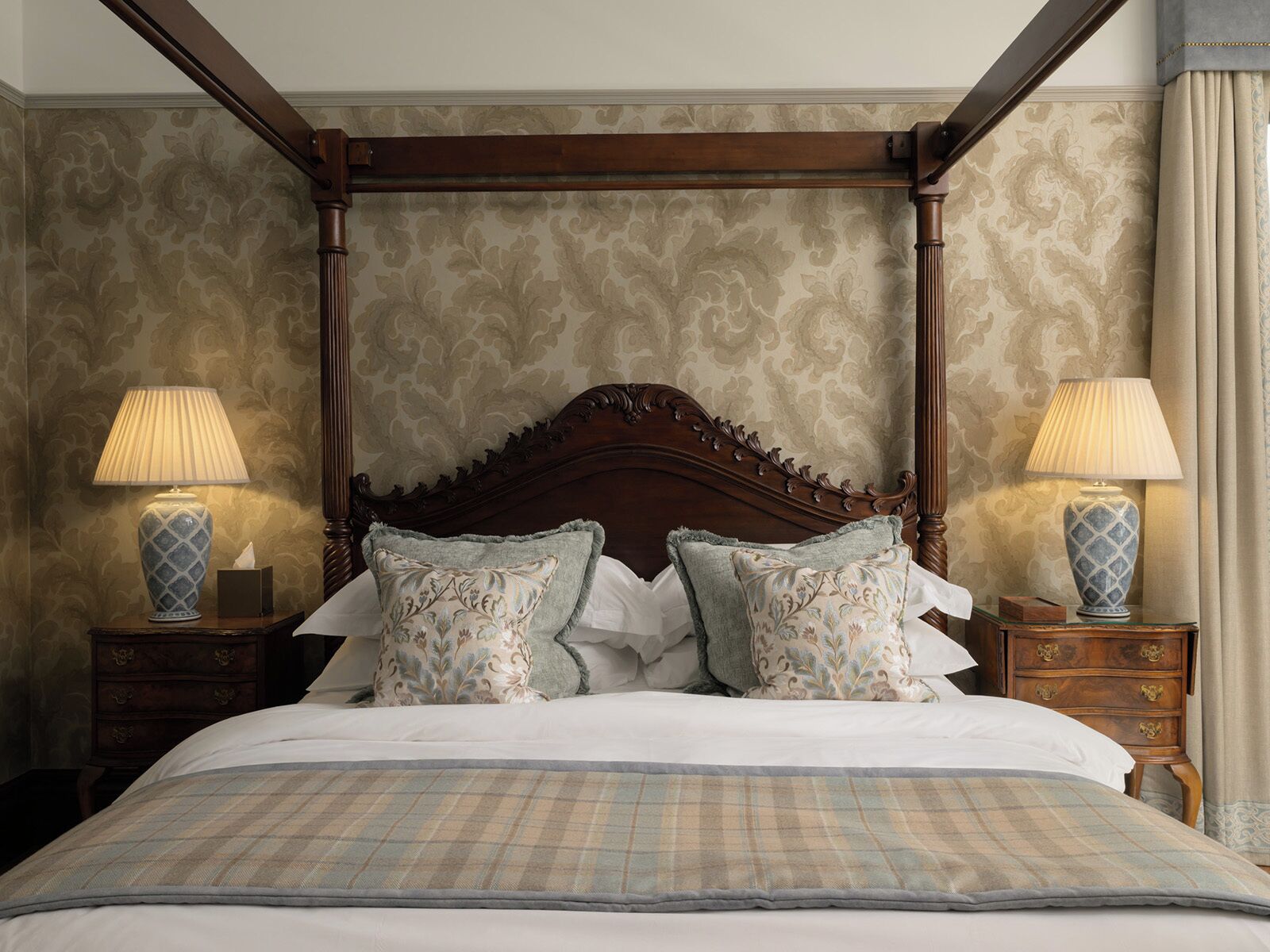A four-poster bed with ornate wooden headboard, two bedside tables with lamps, and floral-patterned pillows.