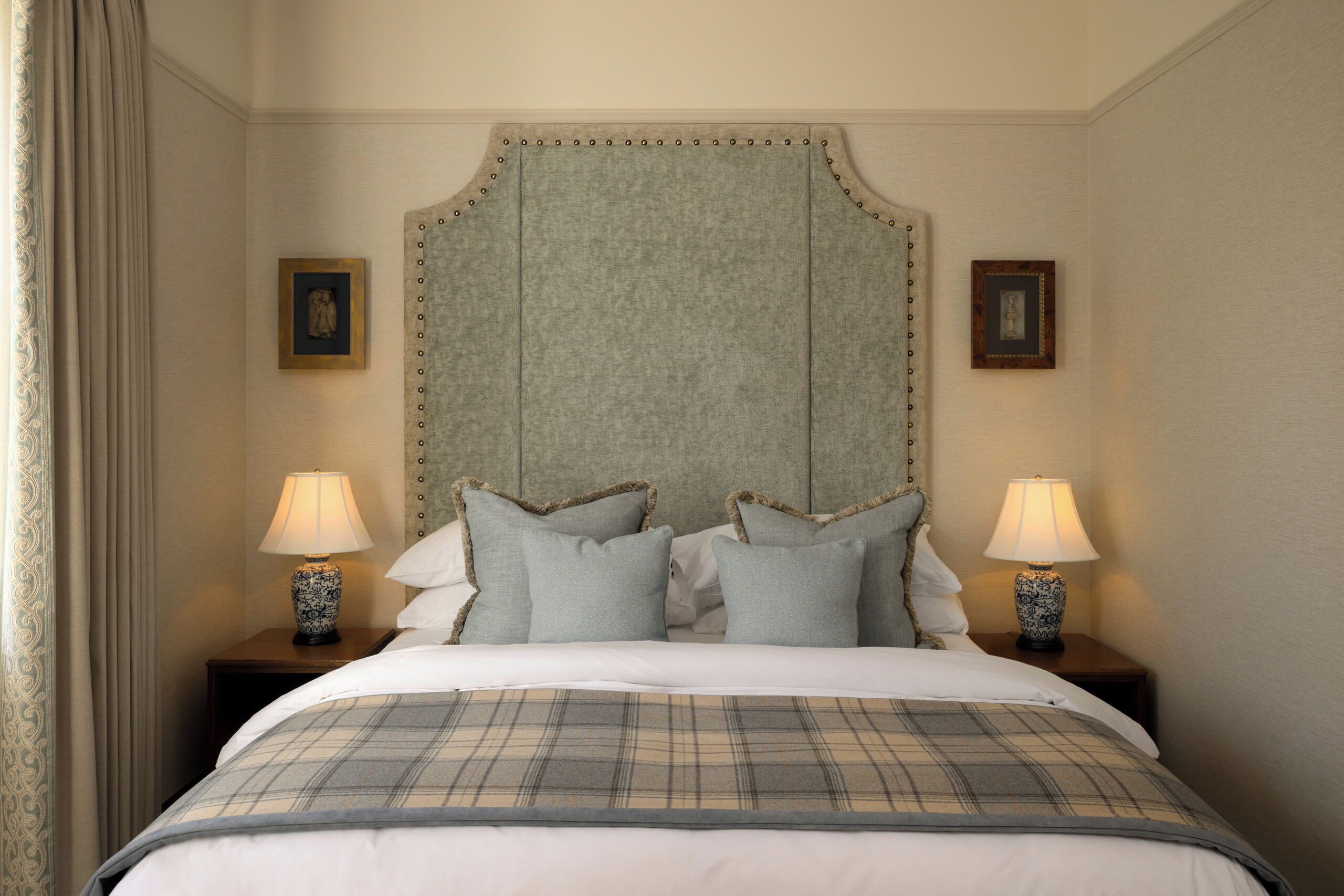 A neatly made bed with a plaid bedspread, two bedside lamps, and a headboard with a decorative trim.