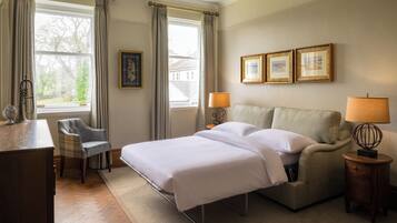 A hotel room with a bed, a chair, a desk, a lamp, and framed pictures on the wall.