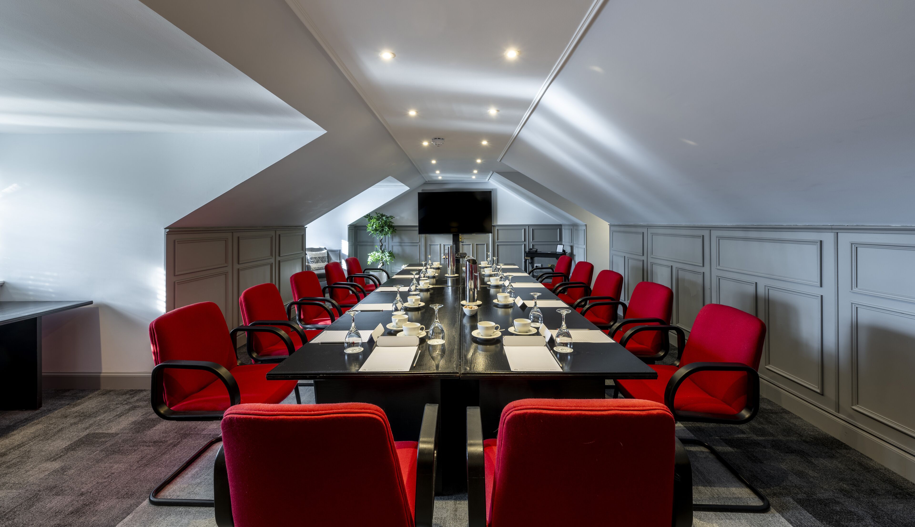 A conference room with a long table, red chairs, and a flat-screen TV.