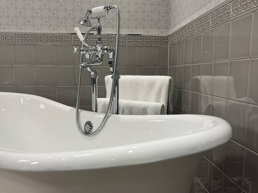 A bathroom with a freestanding bathtub, a towel rack, and patterned tiles.
