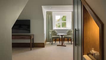 A room with a television, a desk, two chairs, a window with curtains, and a wooden cabinet.