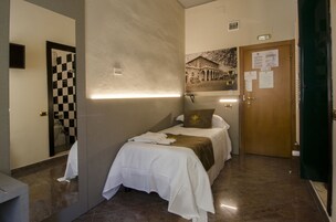Una habitación de hotel con una cama, un espejo de cuadros, una lámpara de pared, una puerta con placa y un cartel en la pared.