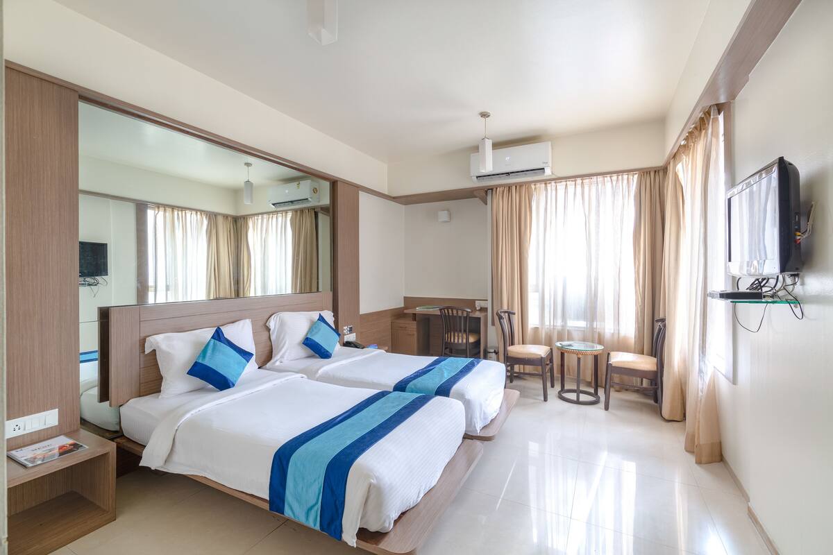 Habitación de hotel con dos camas, un escritorio, una silla, un televisor y aire acondicionado.