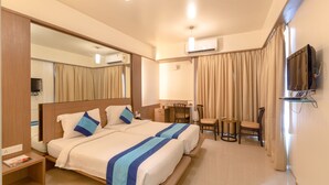 A hotel room with a large bed, a desk, a chair, a TV, and an air conditioning unit. - Ivy Studios Hotel Near Pune Airport (Pune)