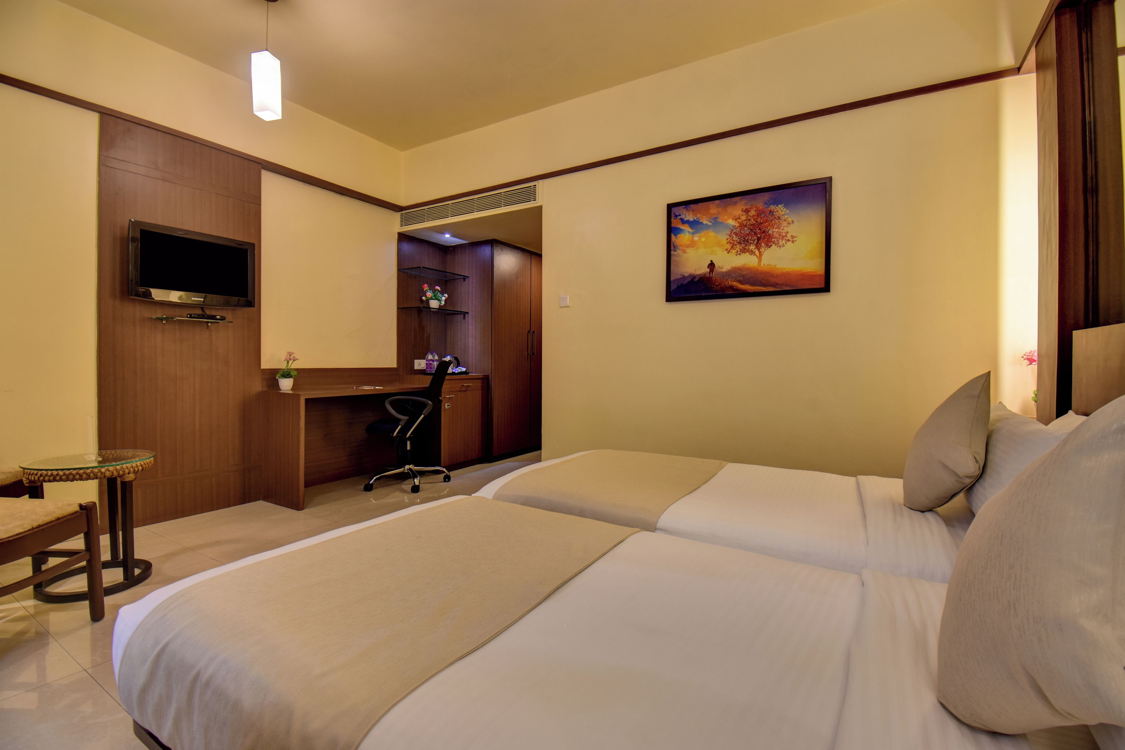 A hotel room with a bed, desk, chair, TV, and artwork on the wall.