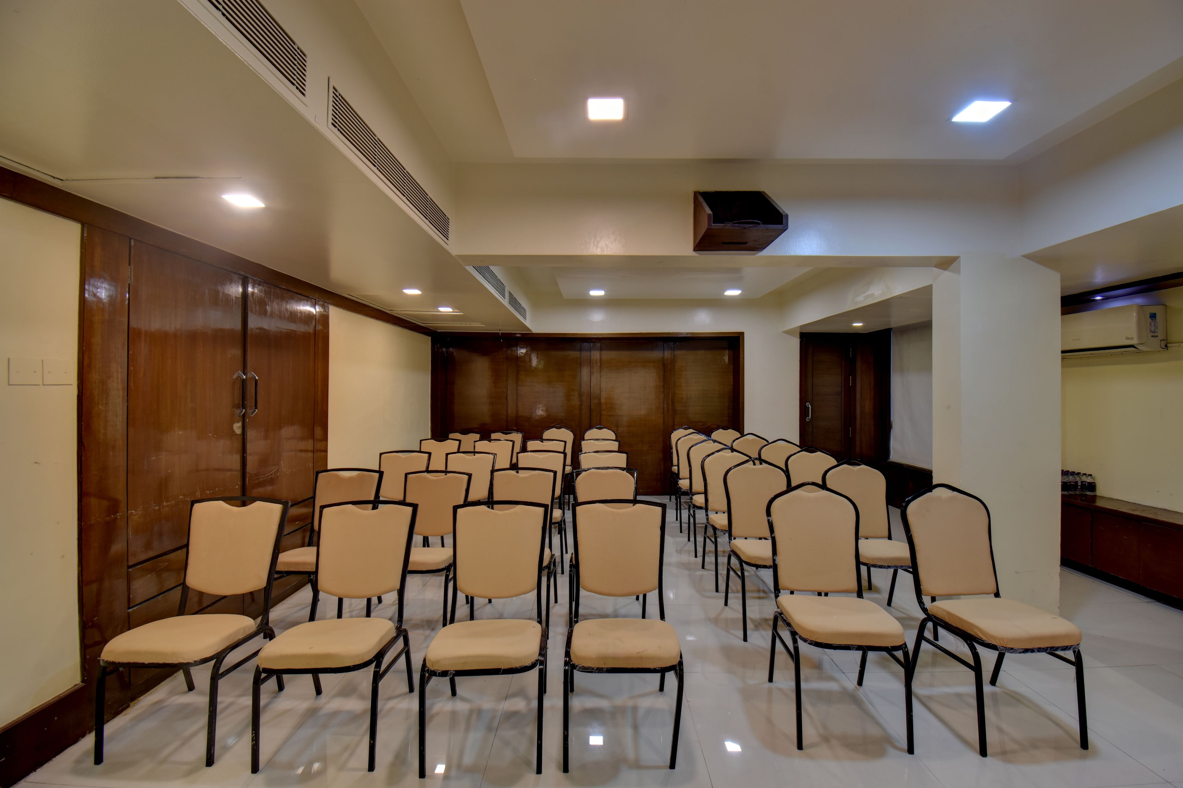 A conference room with rows of chairs, a wooden door, and ceiling vents.