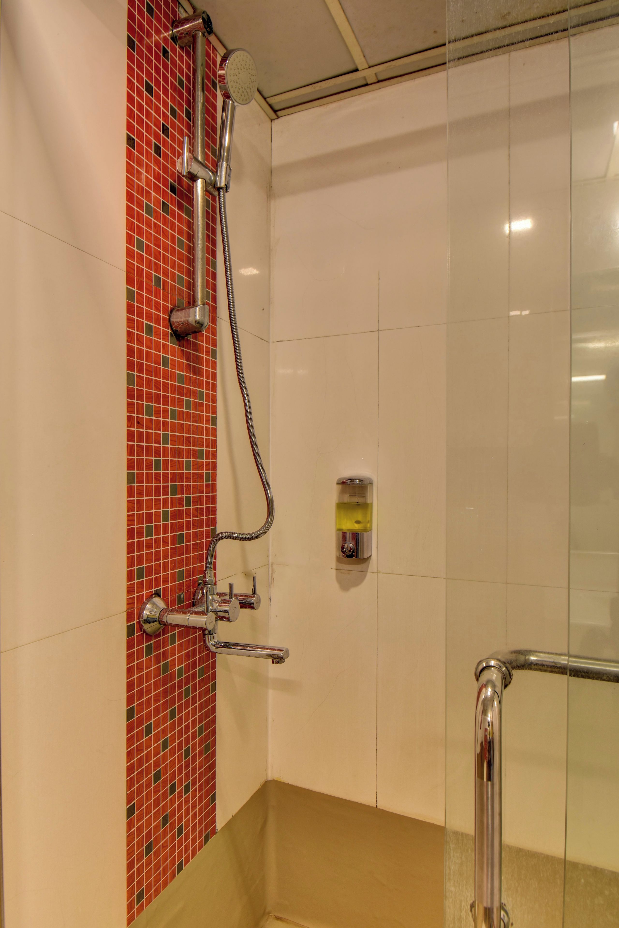 Un angolo doccia con divisorio in vetro, una parete rivestita di piastrelle rosse e una vasca da bagno color beige.
