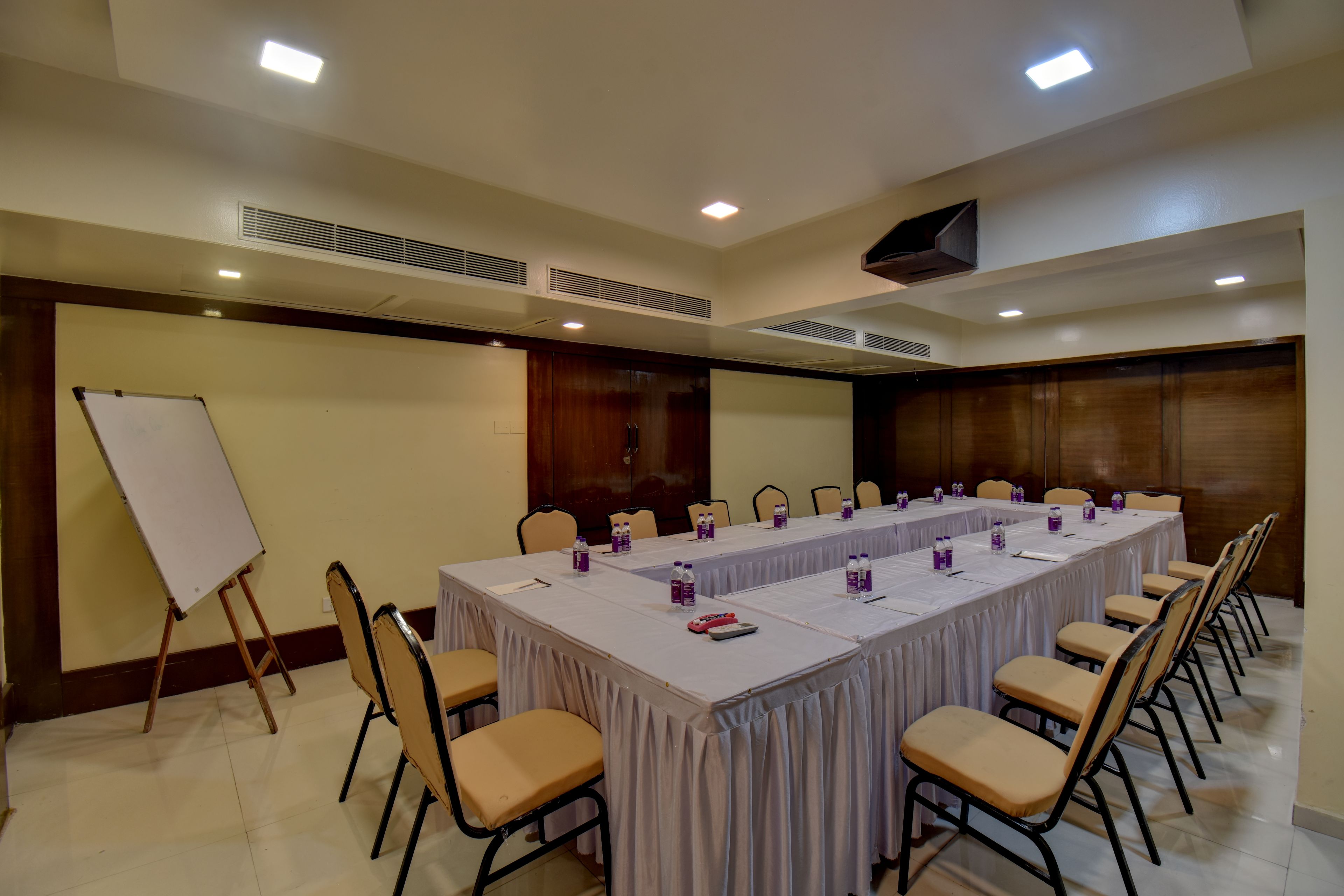 Uma sala de conferências com uma longa mesa, cadeiras, um quadro branco e grelhas no teto.