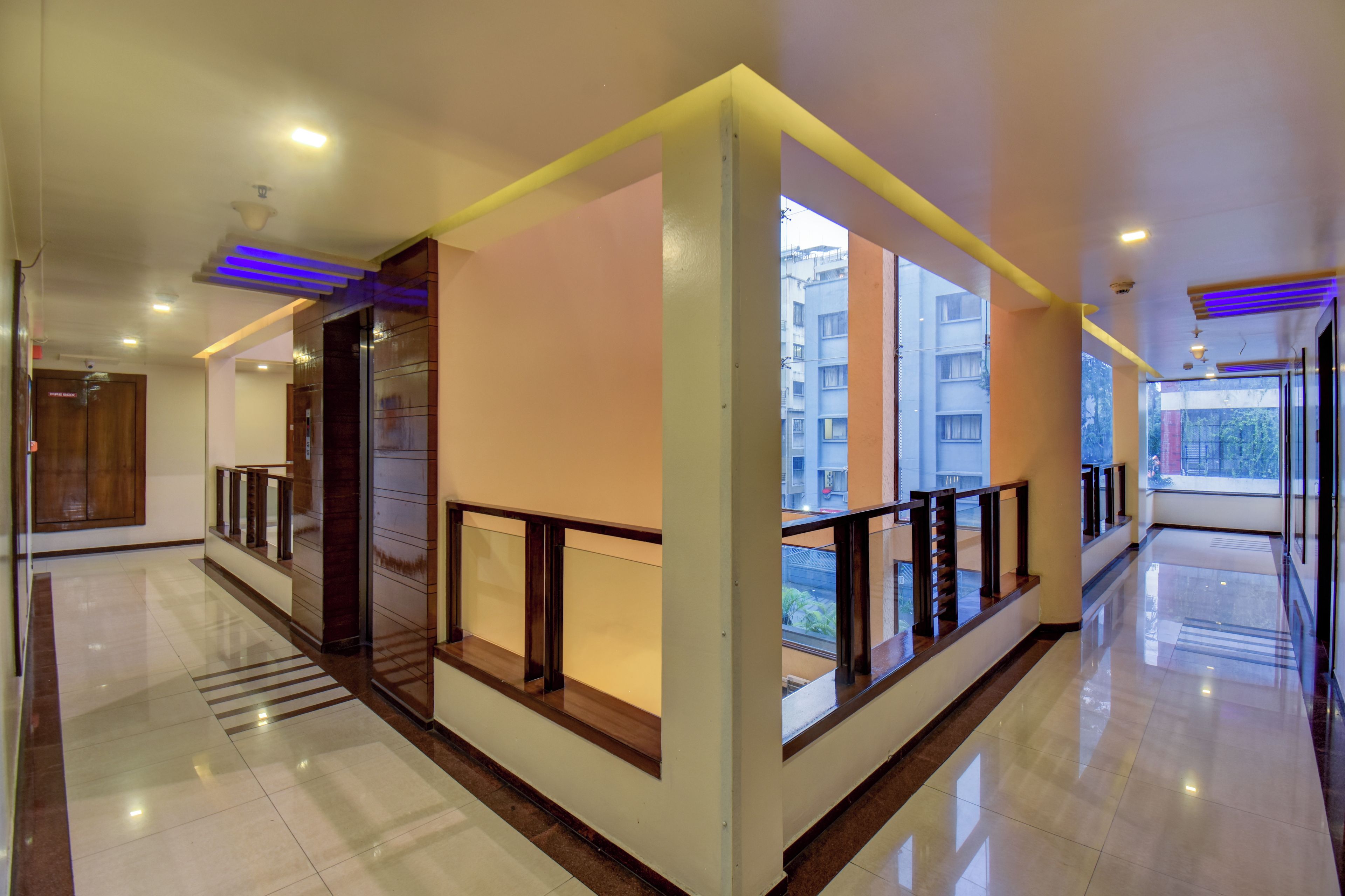 Corredor amplo com guarda-corpo de vidro, lareira e vista para o exterior.
