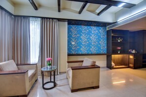 A modern living room with a sofa set, a small round table with a vase, and a blue floral wall. - Hotel Lotus Ivy Studios,Near Pune Airport (Pune)