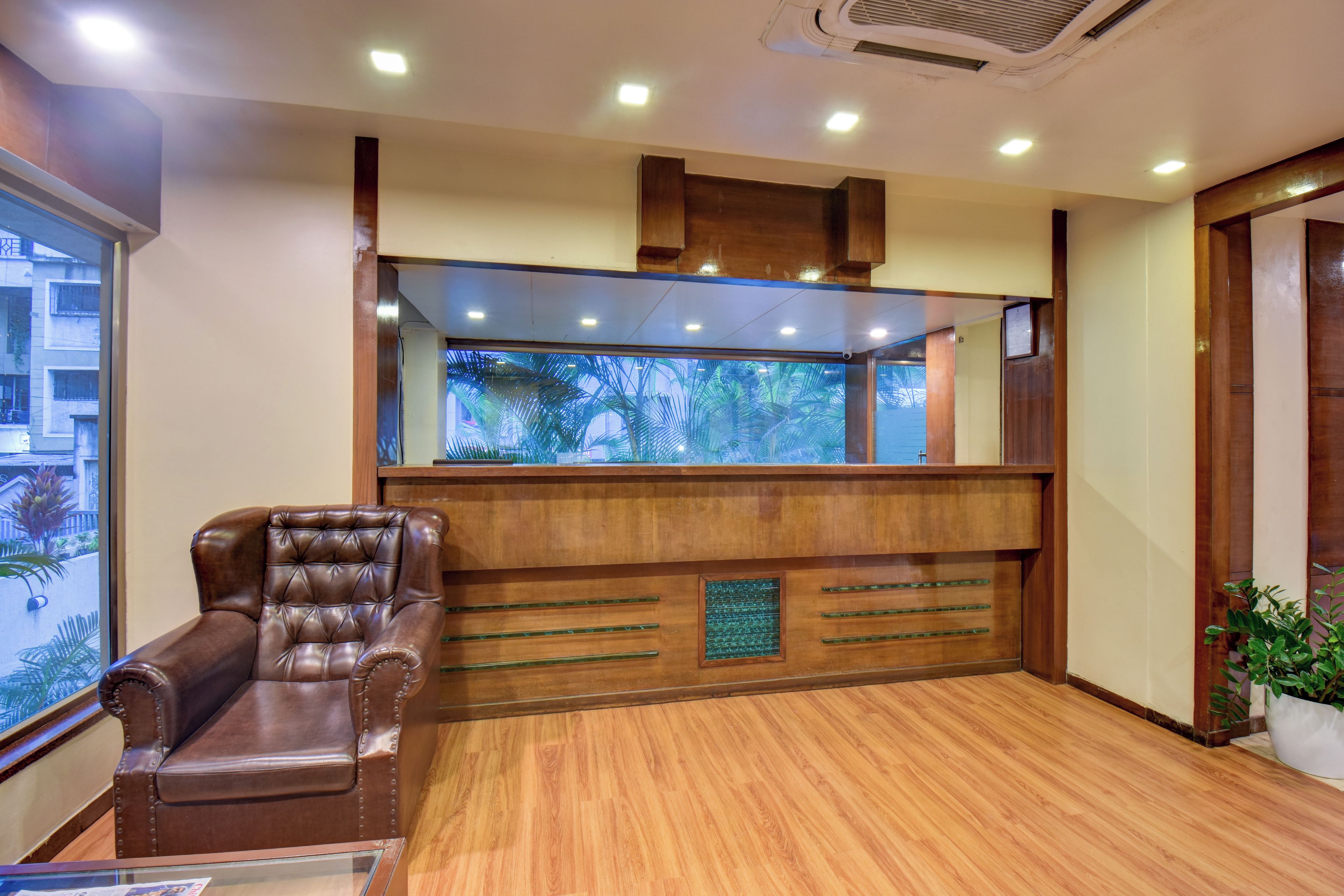 Una habitación con mostrador de recepción de madera, un sillón de cuero y un ventanal con vista a palmeras.