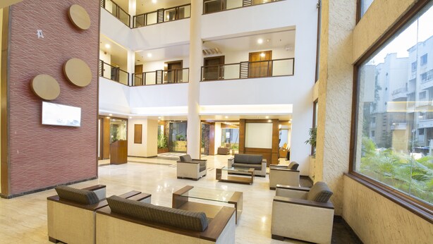 A spacious lobby with multiple seating areas, a large window offering a view of the outside, and a modern architectural design with a high ceiling and multiple floors. - Ivy Studios Hotel Near Pune Airport (Pune)