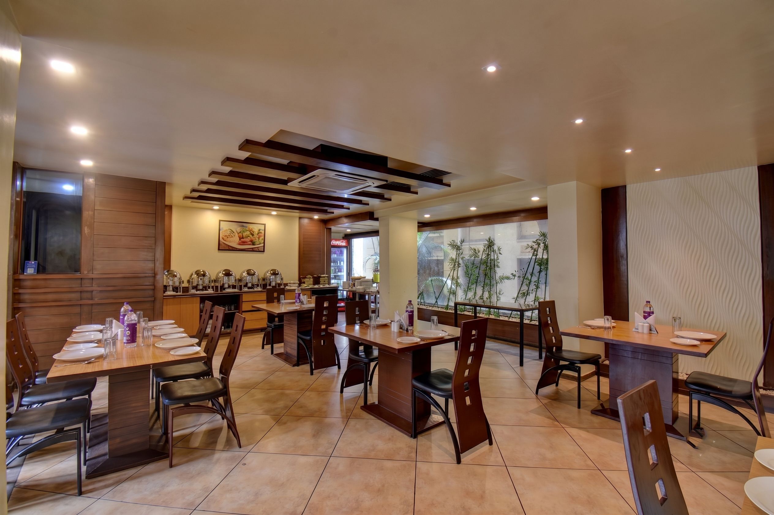 Un restaurante con varias mesas, sillas y un ventanal que ofrece vistas a plantas de bambú.